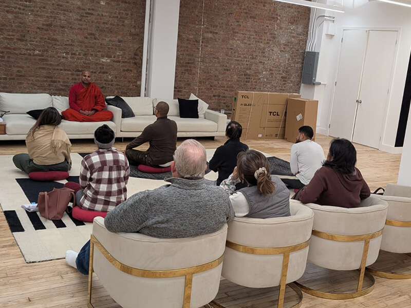 A group seated on cushions and in armchairs listening to a Buddhist monk at a Meditate With A Monk session in Manhattan