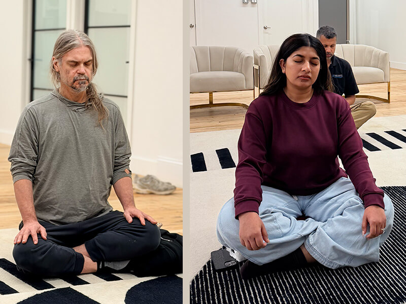 Two participants meditating with eyes closed and hands resting on their knees at a Meditate With A Monk session in New York