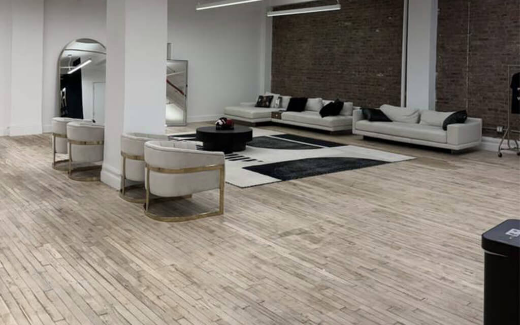 The open loft space at Faces by AKJ, with pale wood floors, white sofas and armchairs, and an exposed brick wall